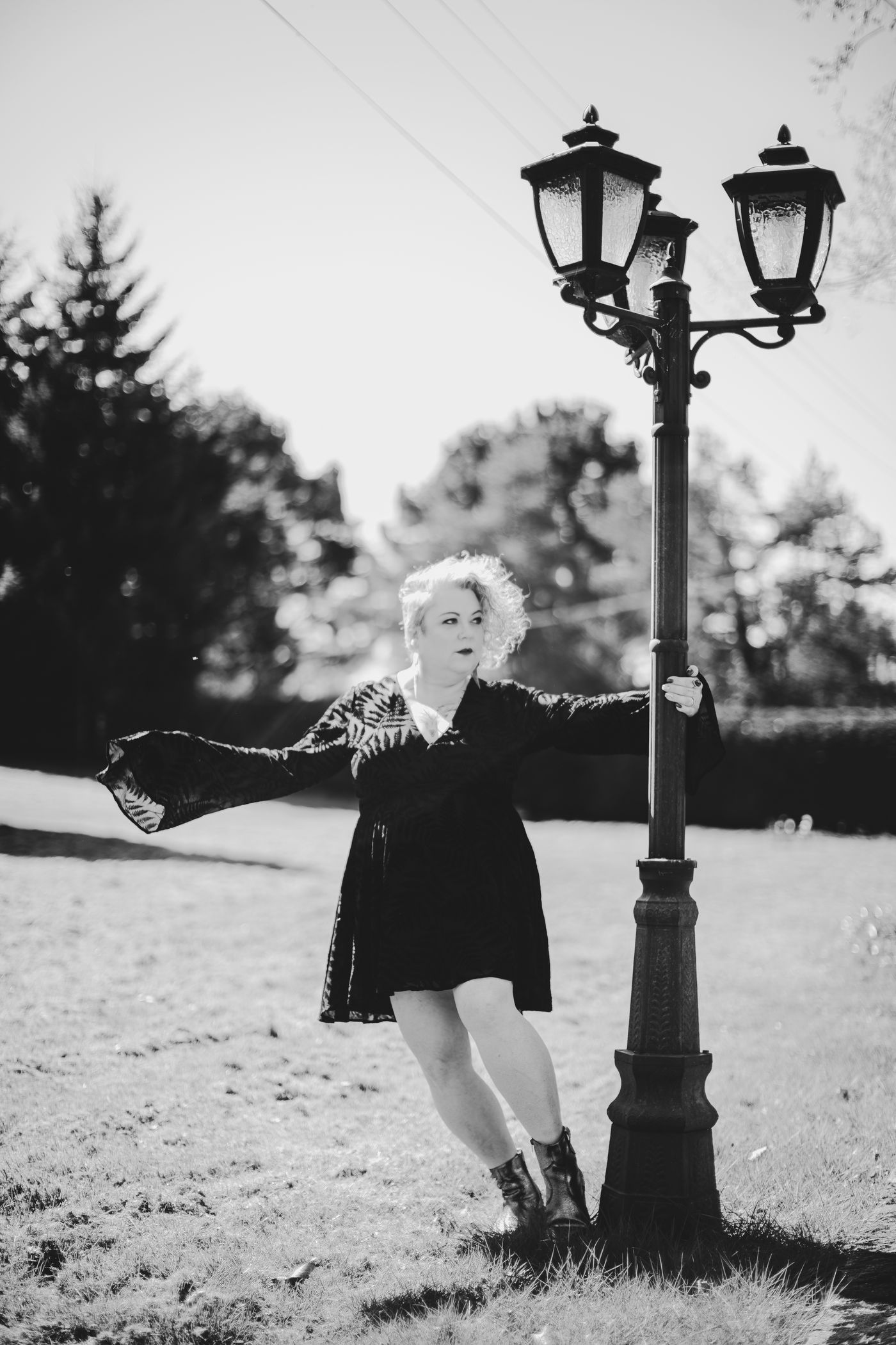 Black and white photo of a woman in a velvet dress with flared sleeves swinging round a vintage lamppost – personality branding by wo0