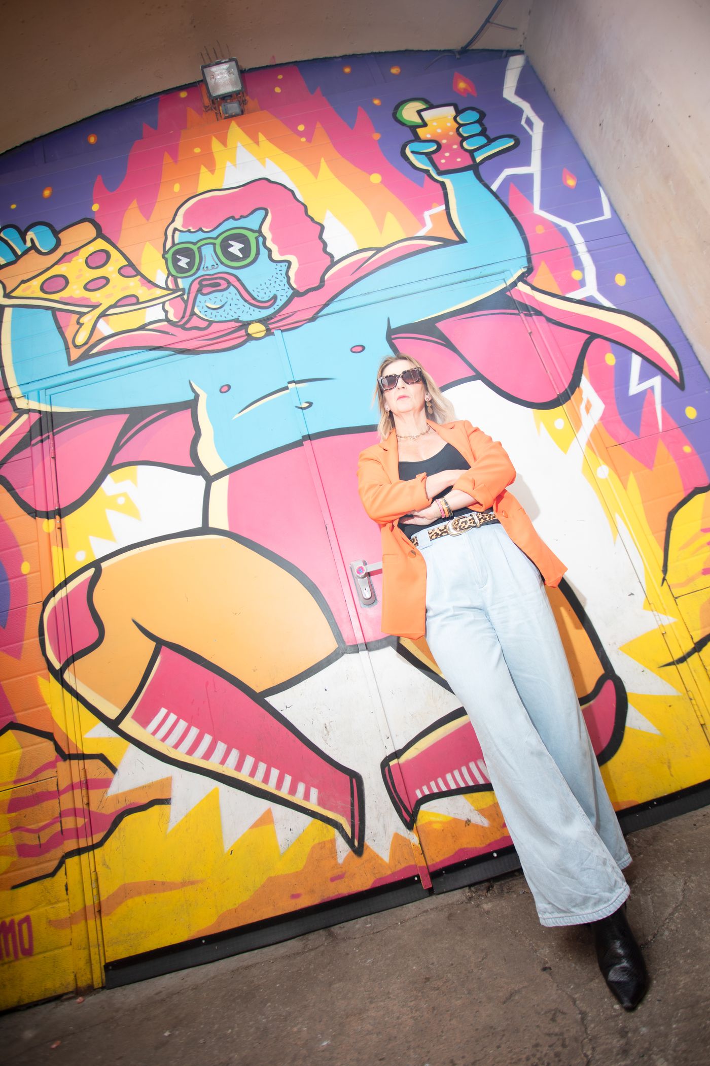 Woman in an orange jacket and wide jeans in front of a bright cartoon mural – personal branding photoshoot by wo0