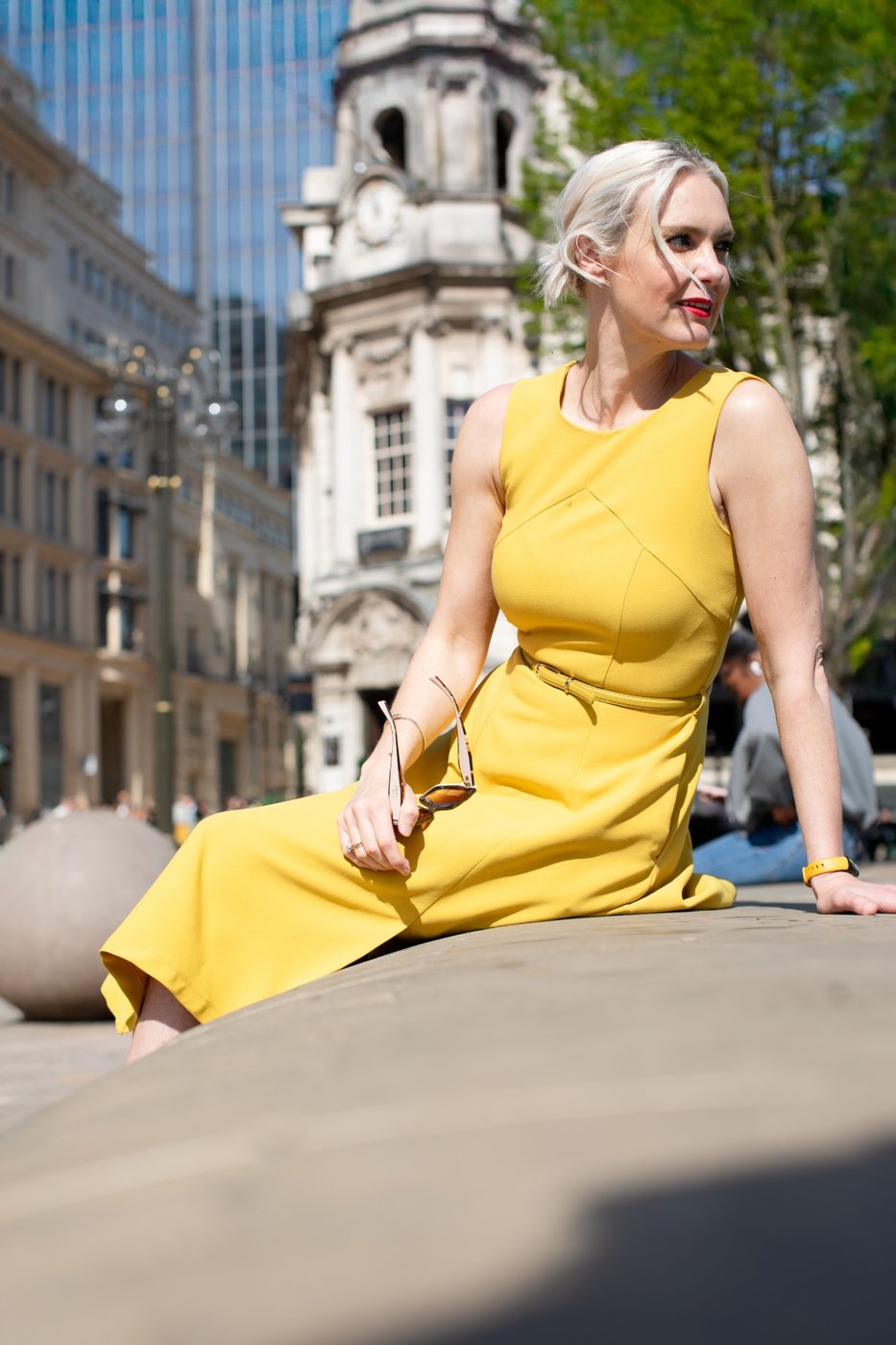 Woman in a yellow dress and red lipstick sitting in a sunny city square – brand photoshoot by wo0