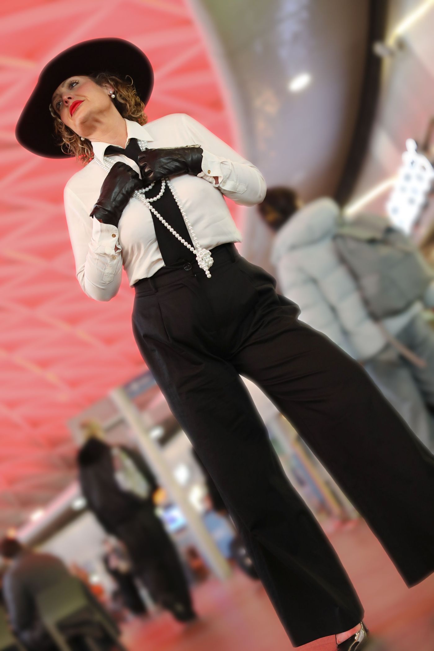 Woman in black wide-leg trousers, white shirt, pearls and a black hat at a fashion event – photographed by wo0