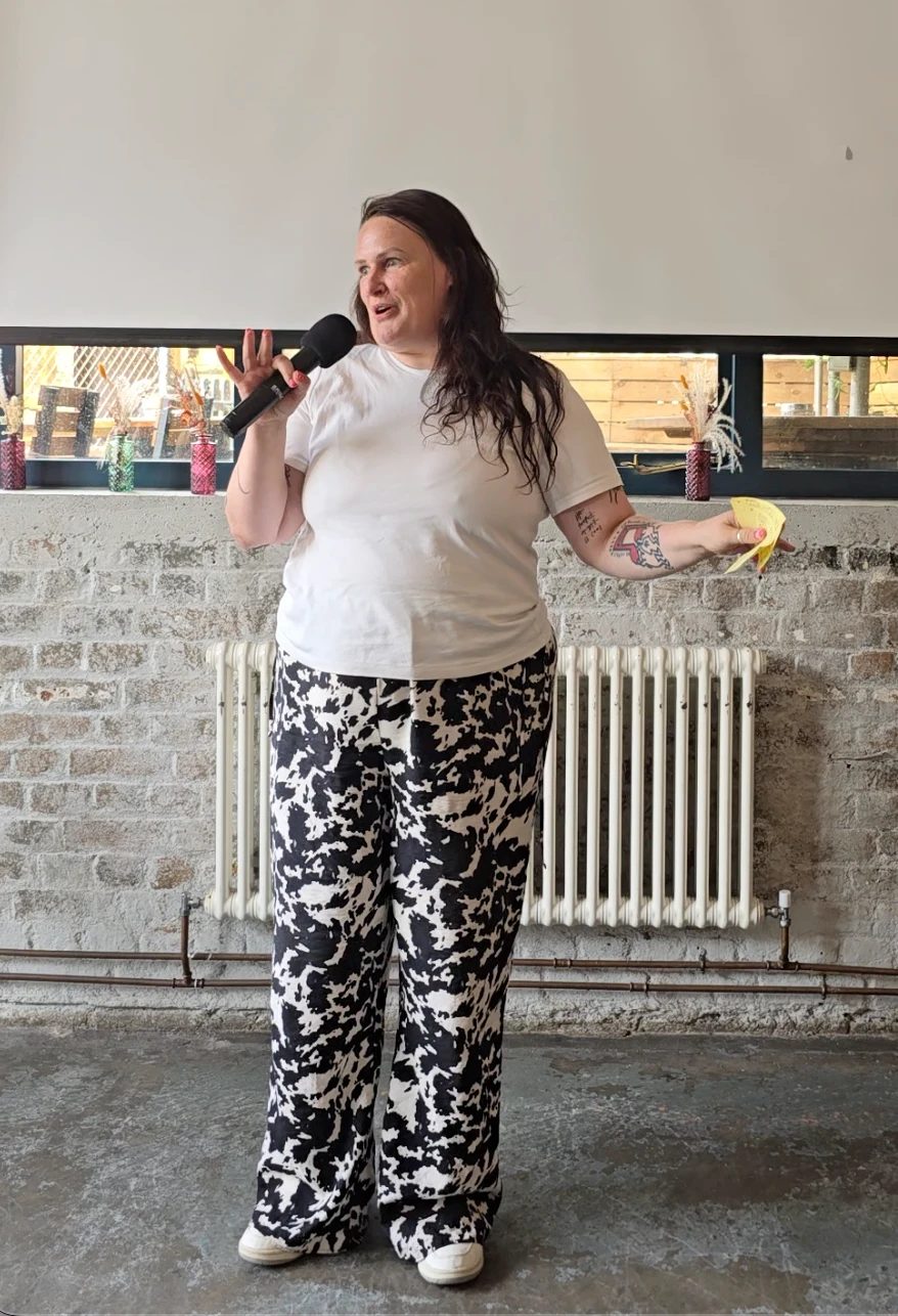 Wendy ‘wo0’ Gannon in a white T-shirt and cow print trousers speaking into a microphone with her notes